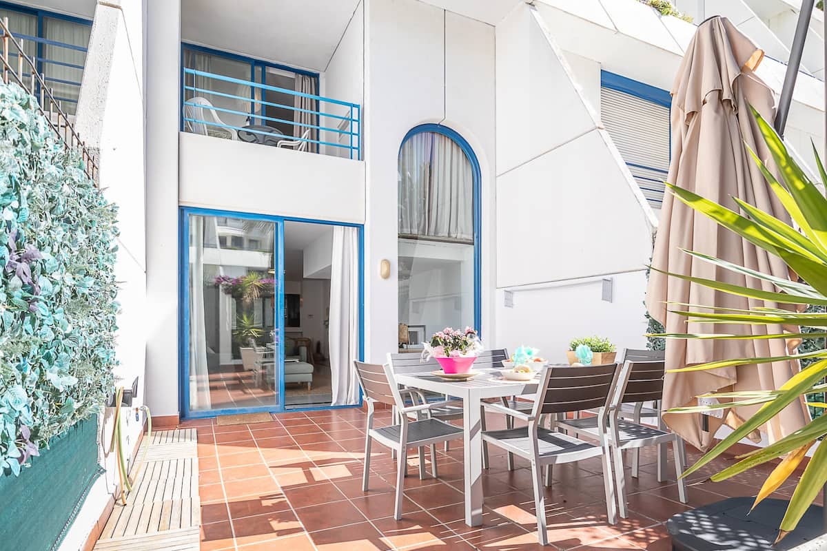 A patio with a table and chairs, a covered area, and a staircase leading to an upper level.