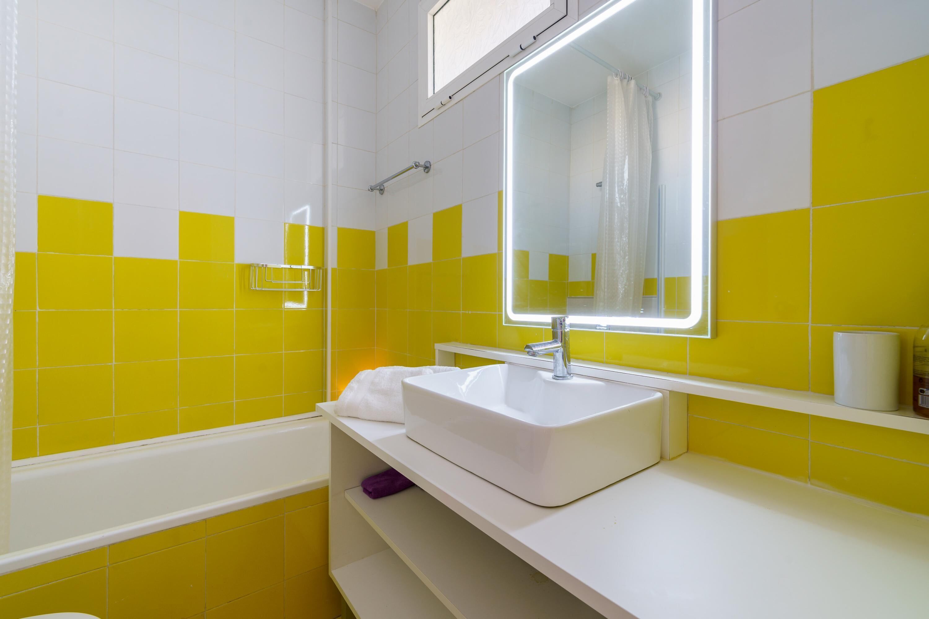 Ein Badezimmer mit einem weißen Waschbecken, gelb-weißen Fliesen, einem Spiegel und einer Duschvorhang.