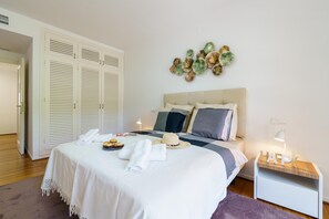 Un lit bien fait, avec une couette blanche, un chapeau et des serviettes sur un plancher en bois.