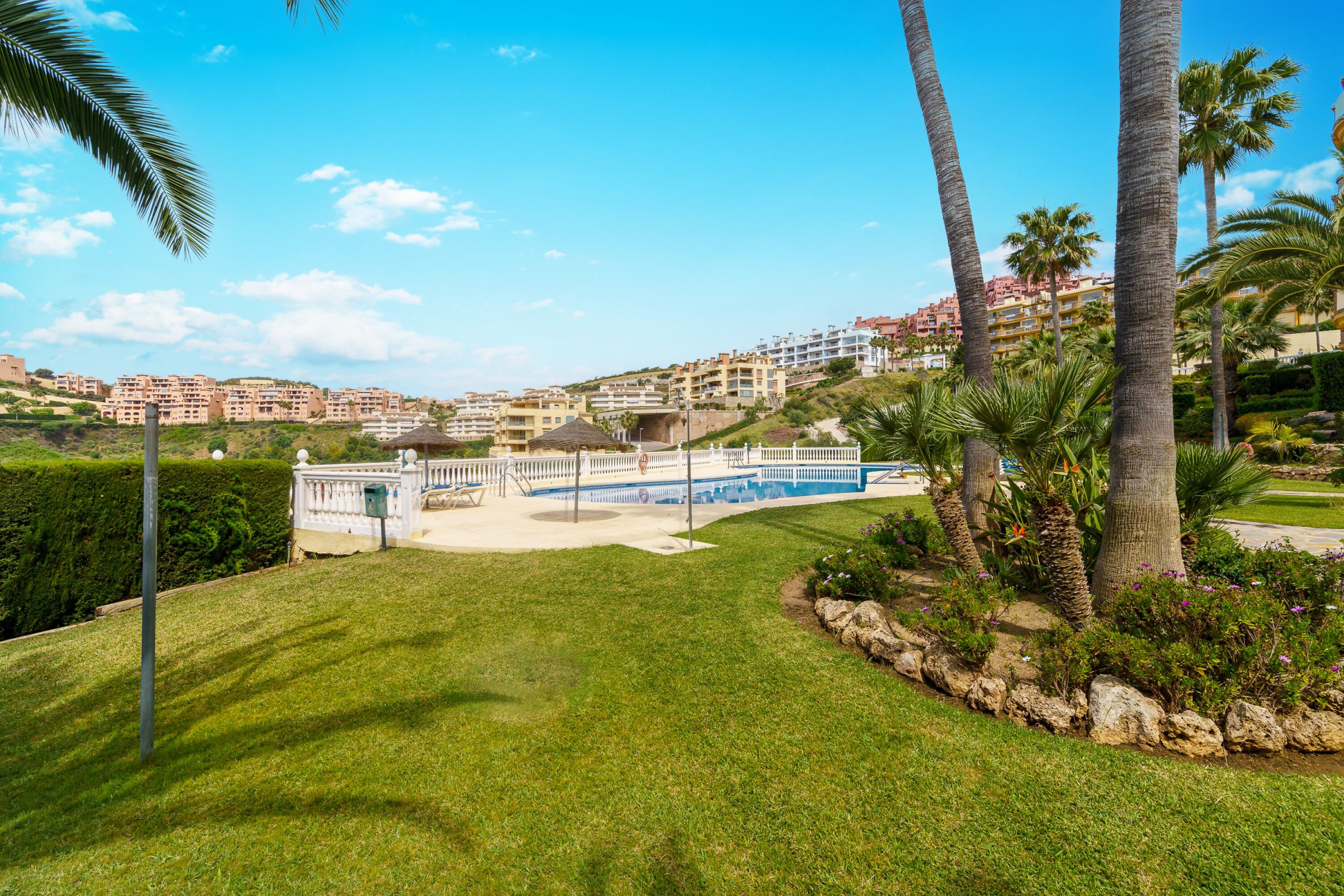 A resort with a pool, palm trees, and a view of the surrounding buildings.