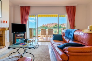 Un salon comprenant un canapé, une table basse en verre, un téléviseur et un balcon offrant une vue sur les immeubles.