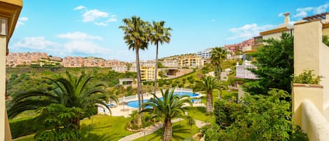 Un resort con piscina, palmeras y vistas a una zona residencial en la ladera.