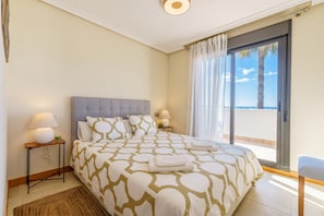 Une chambre avec un grand lit, deux tables de chevet avec des lampes, une vue sur la mer par une porte coulissante et un balcon.