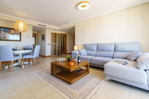 A living room with a wooden coffee table, a grey sofa, and a dining area with chairs and a table. - Sunset Seaview Corner With Pool (Estepona)