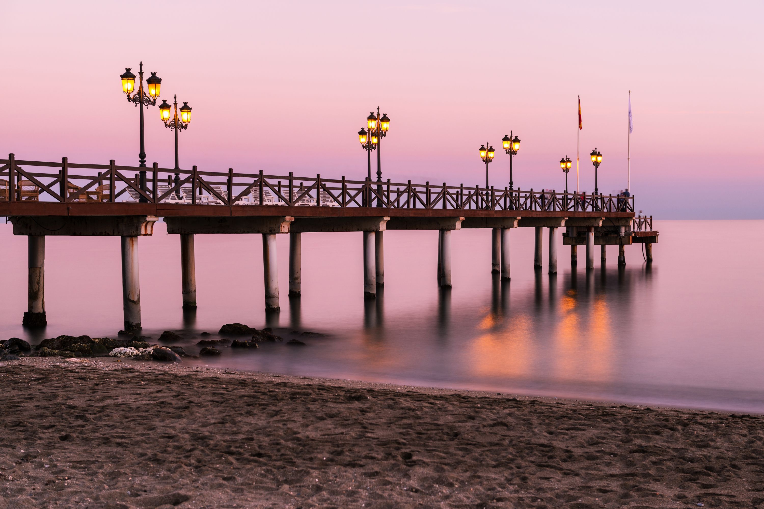 A pier extending into calm waters with evenly spaced street lamps and a railing.