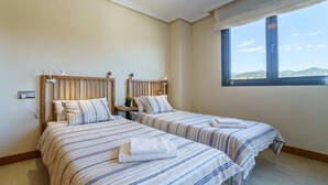 A room with two beds, a window with a view, and a bedside table with a lamp.