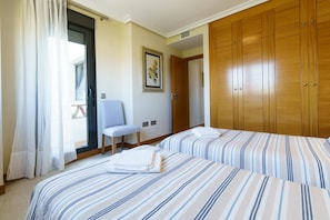 Hotellihuone, jossa on kaksi sänkyä, tuoli, vaatekaappi ja ikkuna, jossa on verhot.