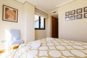 A hotel room with a bed, a chair, a window, and framed pictures on the wall. - Sunset Seaview Corner With Pool (Estepona)
