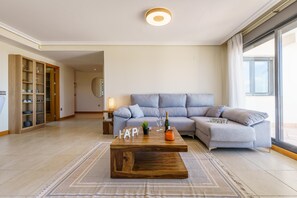 A modern living room with a sectional sofa, a wooden coffee table, and a large window. - Sunset Seaview Corner With Pool (Estepona)
