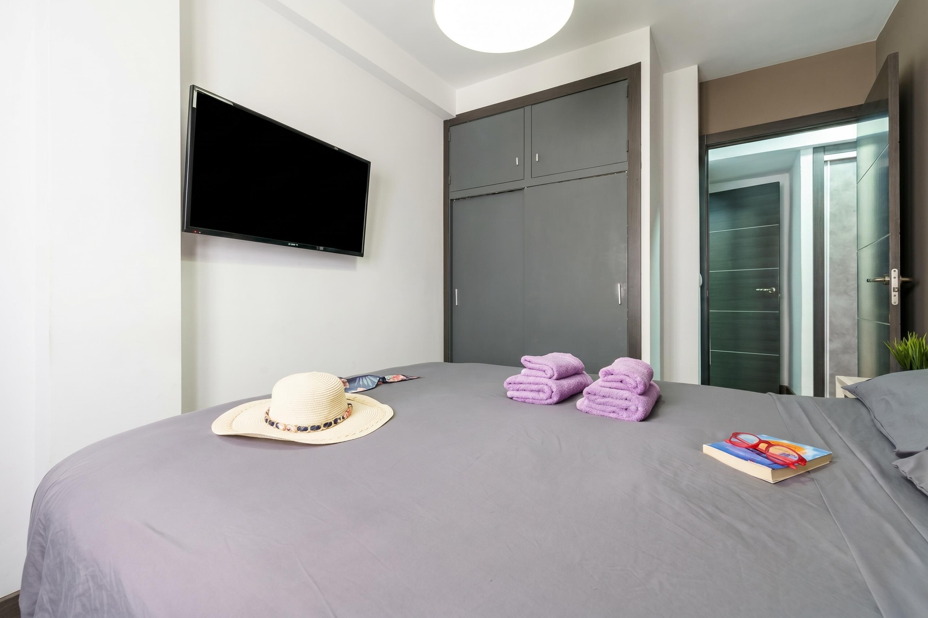 A modern hotel room with a bed, a television, a wardrobe, and a bathroom door.