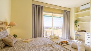 Ein Hotelzimmer mit Bett, Schreibtisch, Stuhl, einem Balkon mit Blick und einer kleinen Pflanze.