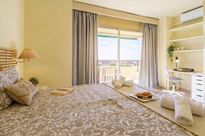 Hotelkamer met een bed, bureau, stoel, balkon met uitzicht en een kleine plant.