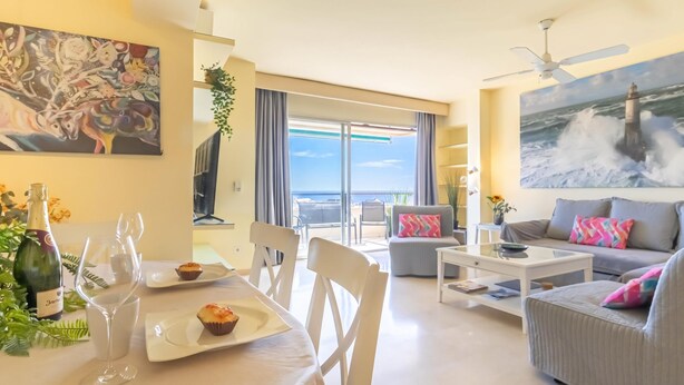 Ein modernes Wohnzimmer mit Essbereich, ein Balkon mit Meerblick und einem Bild an der Wand.