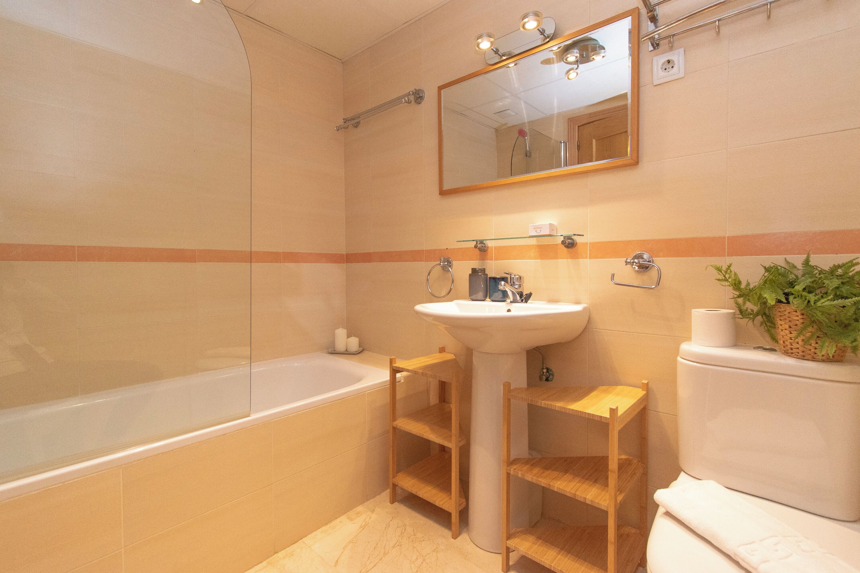 A modern bathroom with a bathtub, a sink, and a toilet. There are wooden shelves and a mirror above the sink.