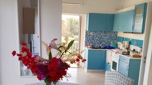Un coin repas avec une table dressée pour deux personnes, un vase de fleurs et une vue sur une cuisine aux armoires bleues.