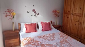 Une chambre à coucher comprenant un lit, deux tables de chevet, une armoire en bois et des éléments de décoration murale, notamment des papillons et des fleurs.