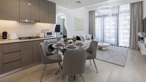 Une cuisine moderne équipée d’appareils électroménagers en acier inoxydable, un coin repas avec une table en verre et un espace de vie doté d’une grande fenêtre et de rideaux.