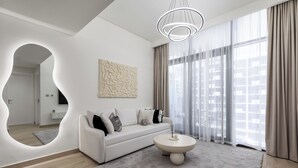 Un salon moderne avec un canapé blanc, une table basse ronde et une grande fenêtre avec des rideaux.