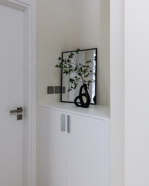 Eine weiße Tür mit silbernem Griff, ein weißes Schranksystem mit silbernen Griffen und eine schwarze Vase mit einer Pflanze darauf.