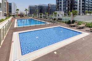 Ein Dachpool mit Liegestühlen und Palmen, umgeben von modernen Gebäuden.