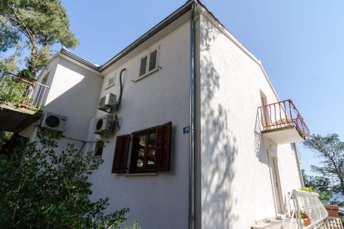 A two-story building with a balcony, air conditioning units, and a small window with shutters.