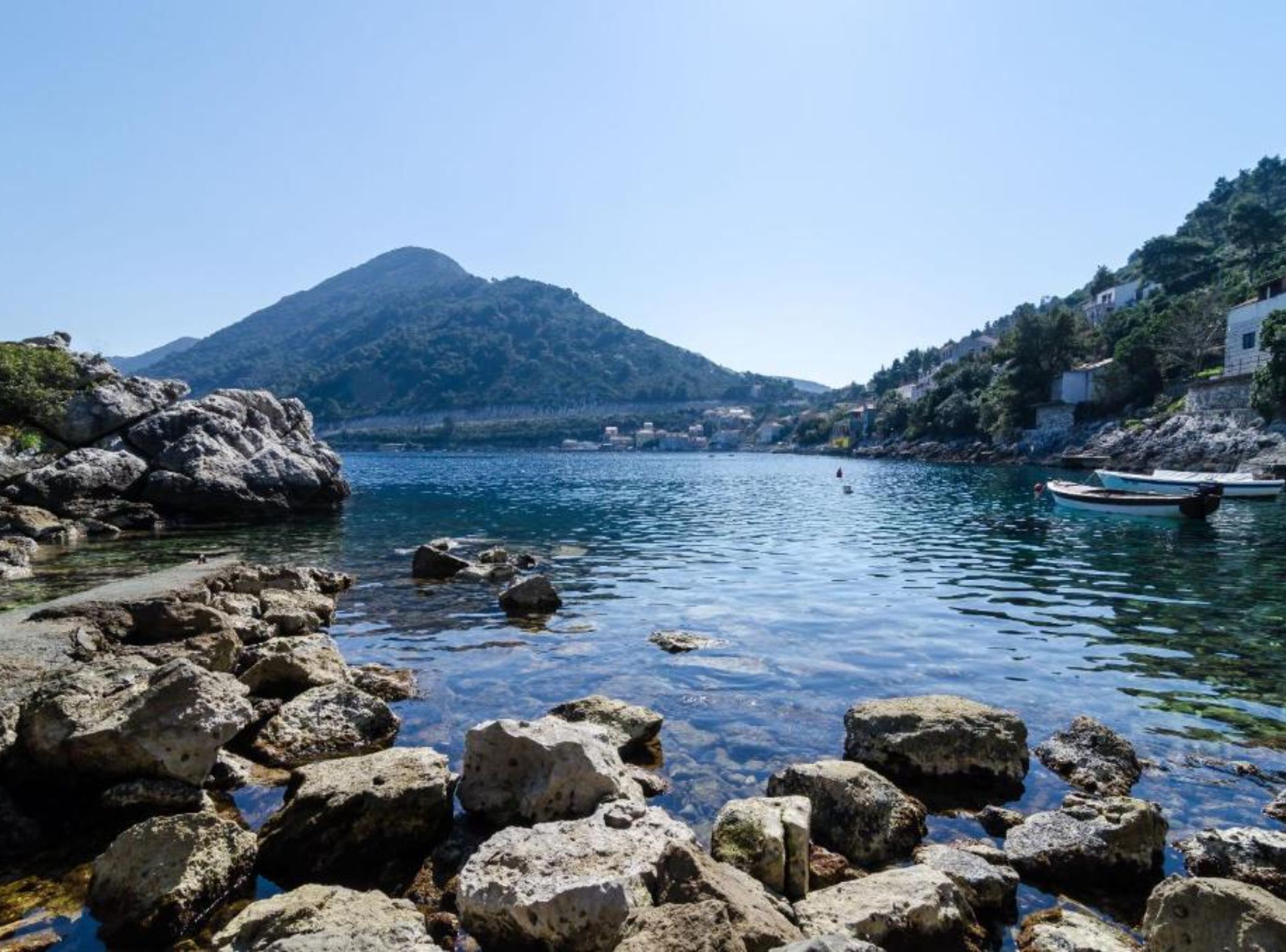 A coastal scene with rocky shores, calm water, and a mountain in the background.