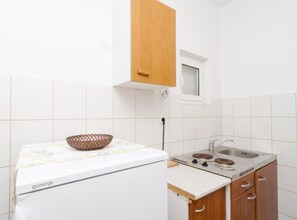 A kitchen with white tiles, a wooden cabinet, a stove, and a sink. - Guest House Sobra 38 (Mljet)