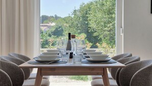 A dining table set with plates, glasses, and a bottle, surrounded by chairs, with a view of greenery and buildings outside. - Villa Onda with private pool and BBQ near Rovinj (Rovinjsko Selo)