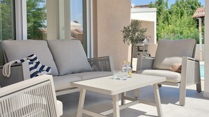 A sunlit outdoor seating area with a sofa, chairs, and a table, featuring a view of a pool and greenery. - Villa Onda with private pool and BBQ near Rovinj (Rovinjsko Selo)