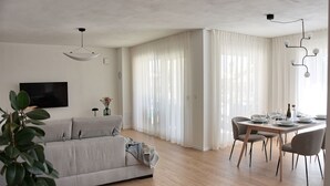 A modern living room with a grey sofa, a dining table set for four, and a large window with sheer curtains. - Villa Onda with private pool and BBQ near Rovinj (Rovinjsko Selo)