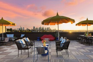 Terraza en la azotea con mesas al aire libre, sombrillas y vistas del horizonte urbano al atardecer.