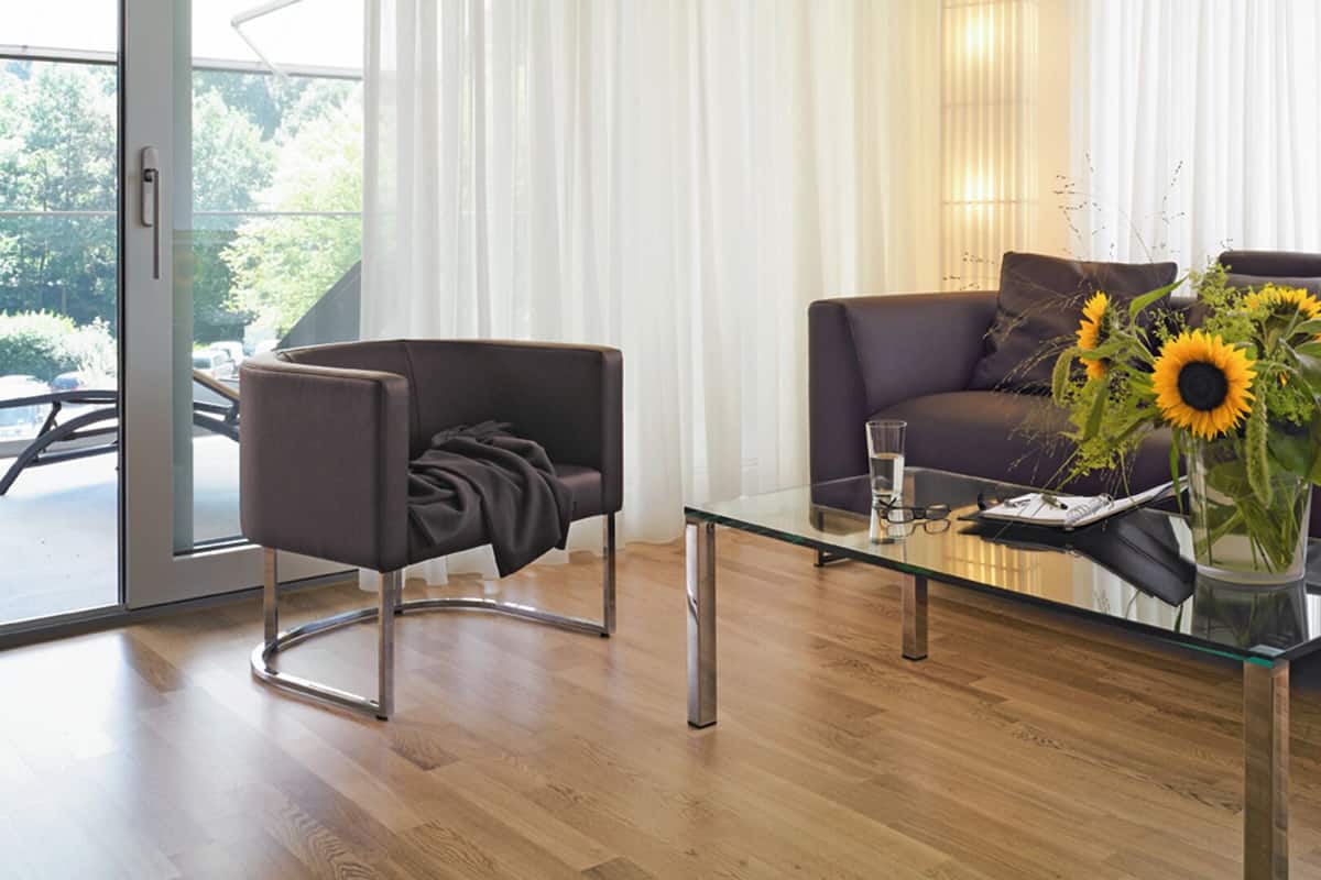 A modern living room with a glass coffee table, a sofa, a chair, and a vase with sunflowers.