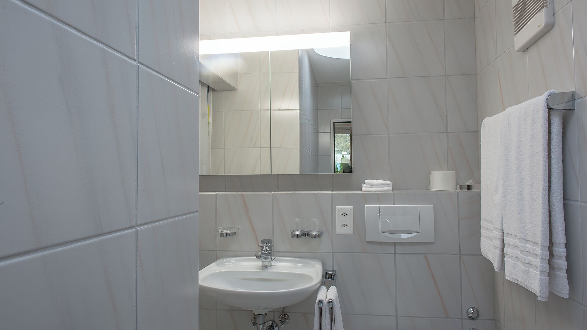 Ein modernes Badezimmer mit Waschbecken, Spiegel, Handtuchhalter und Wandheizung.