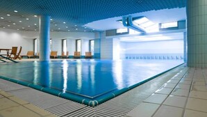 En indendørs swimmingpool med fliset gulv, loft med blåt mønster og havudsigt gennem store vinduer.