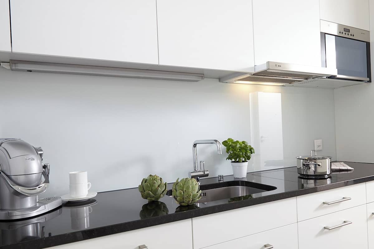 A modern kitchen with white cabinets, a black countertop, a coffee machine, a sink, a potted plant, and a pot on the counter.