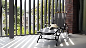 En balkon med stol og bord, udsigt til bygninger og træer, samt en murstensmur.