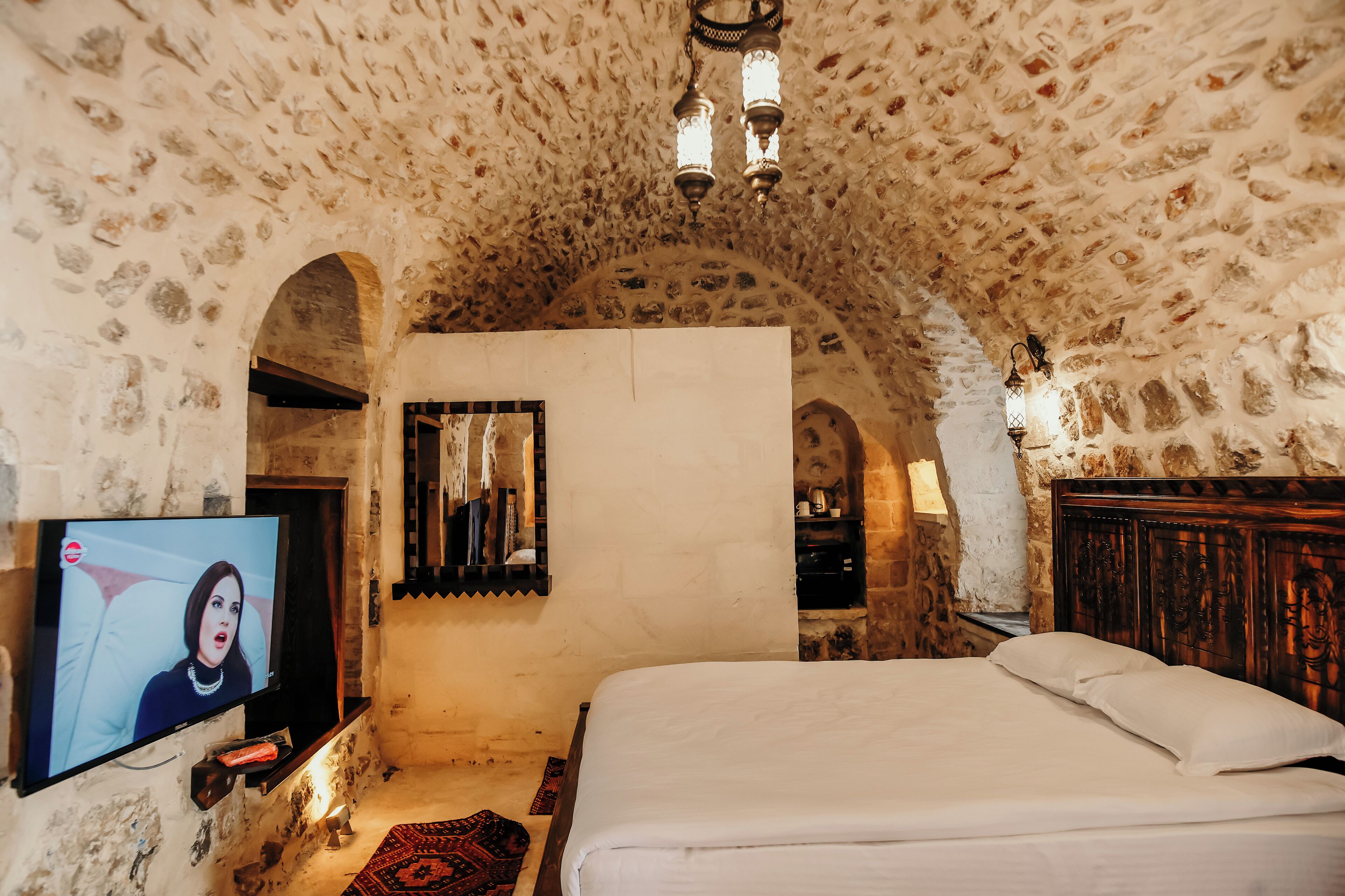 A bedroom with a stone ceiling, a bed, a television, and a wooden headboard.