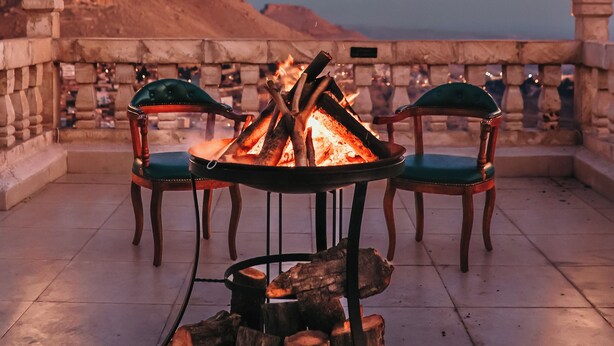 Ein Feuerkorb mit Stühlen und einer Laterne auf einer Terrasse mit Blick auf ein Gebirge.