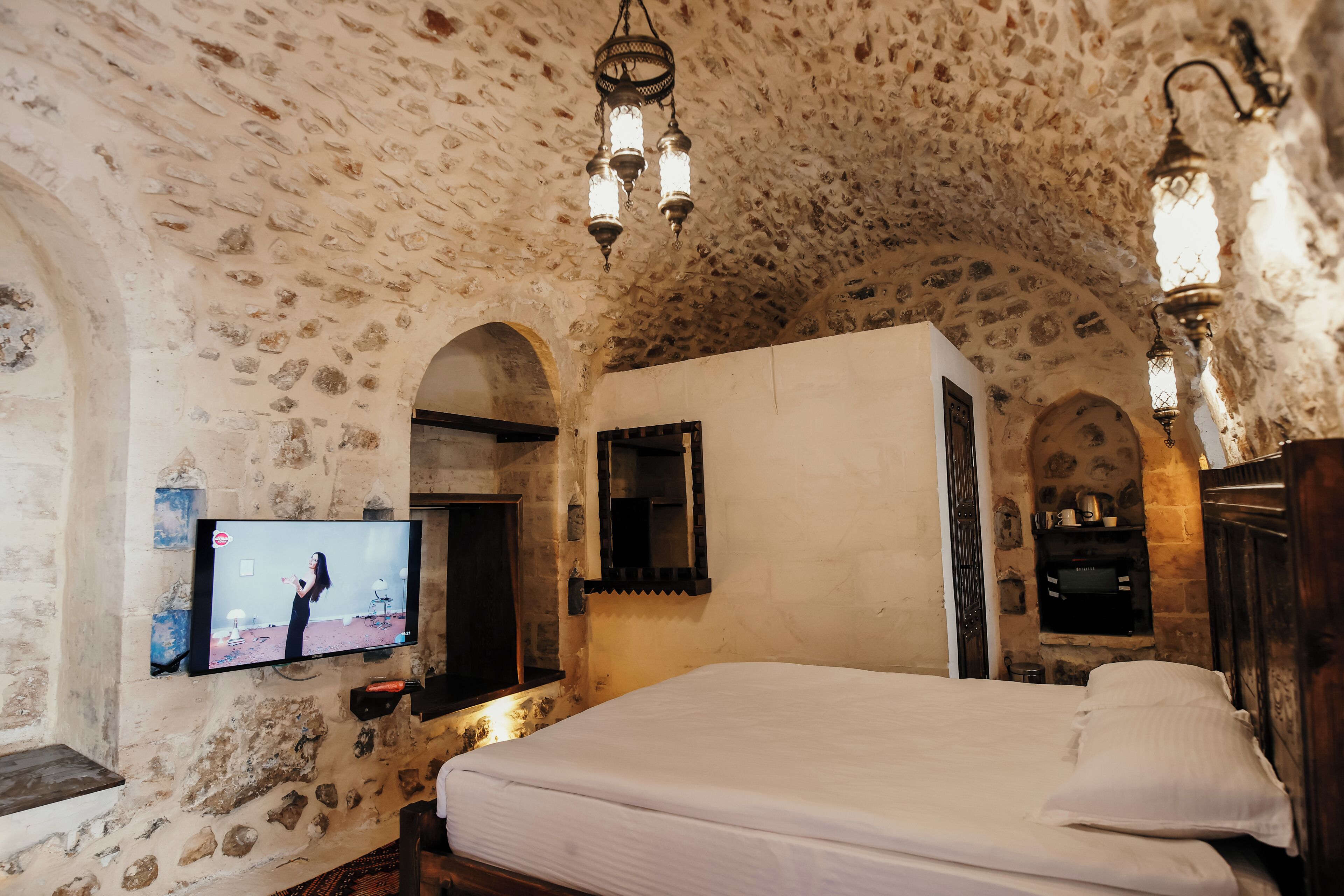 Una habitación con paredes de piedra, una cama, un televisor montado y un armario de madera.