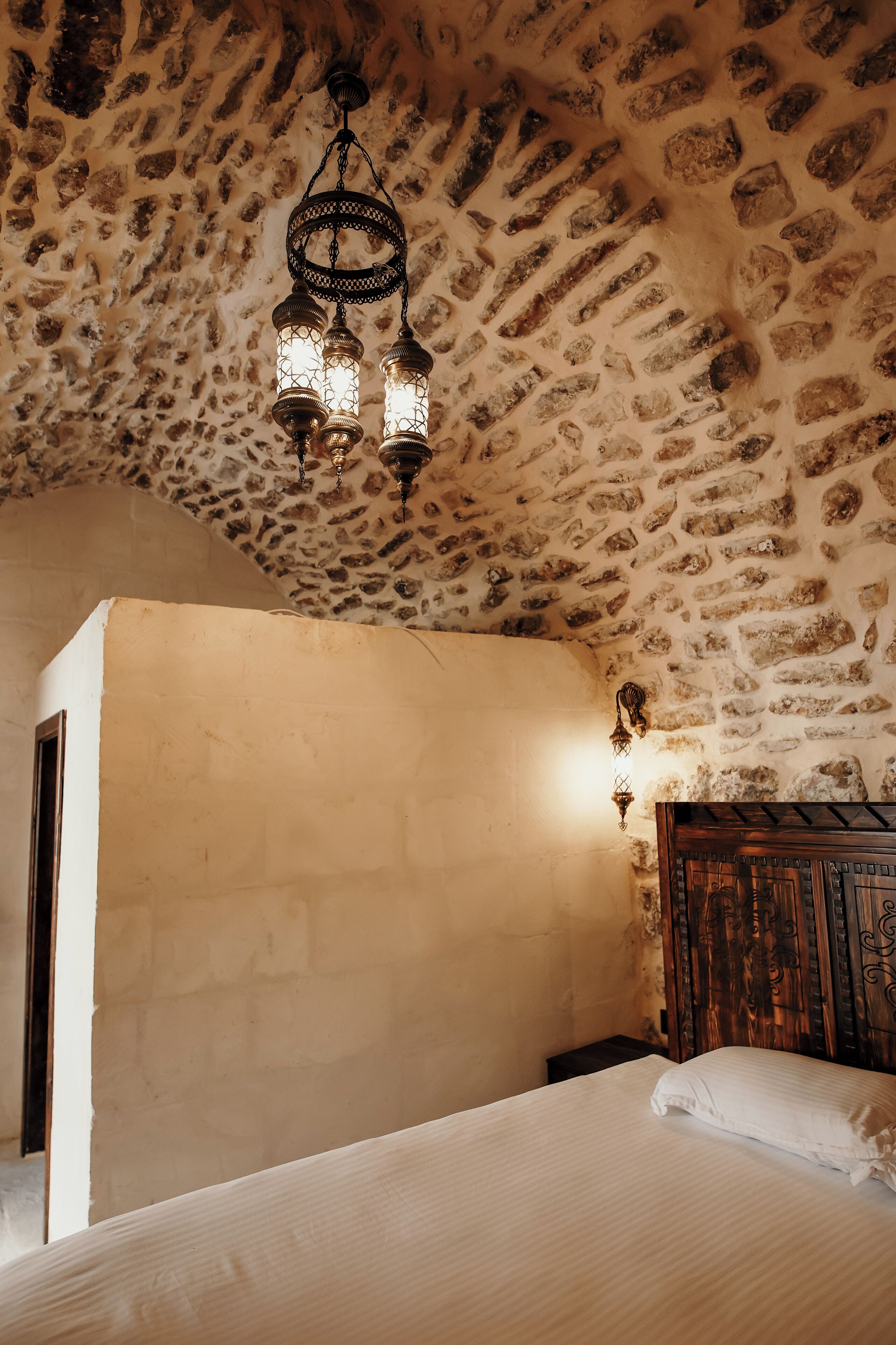 Un dormitorio con techo de piedra, cabecera de madera y lámpara colgante.