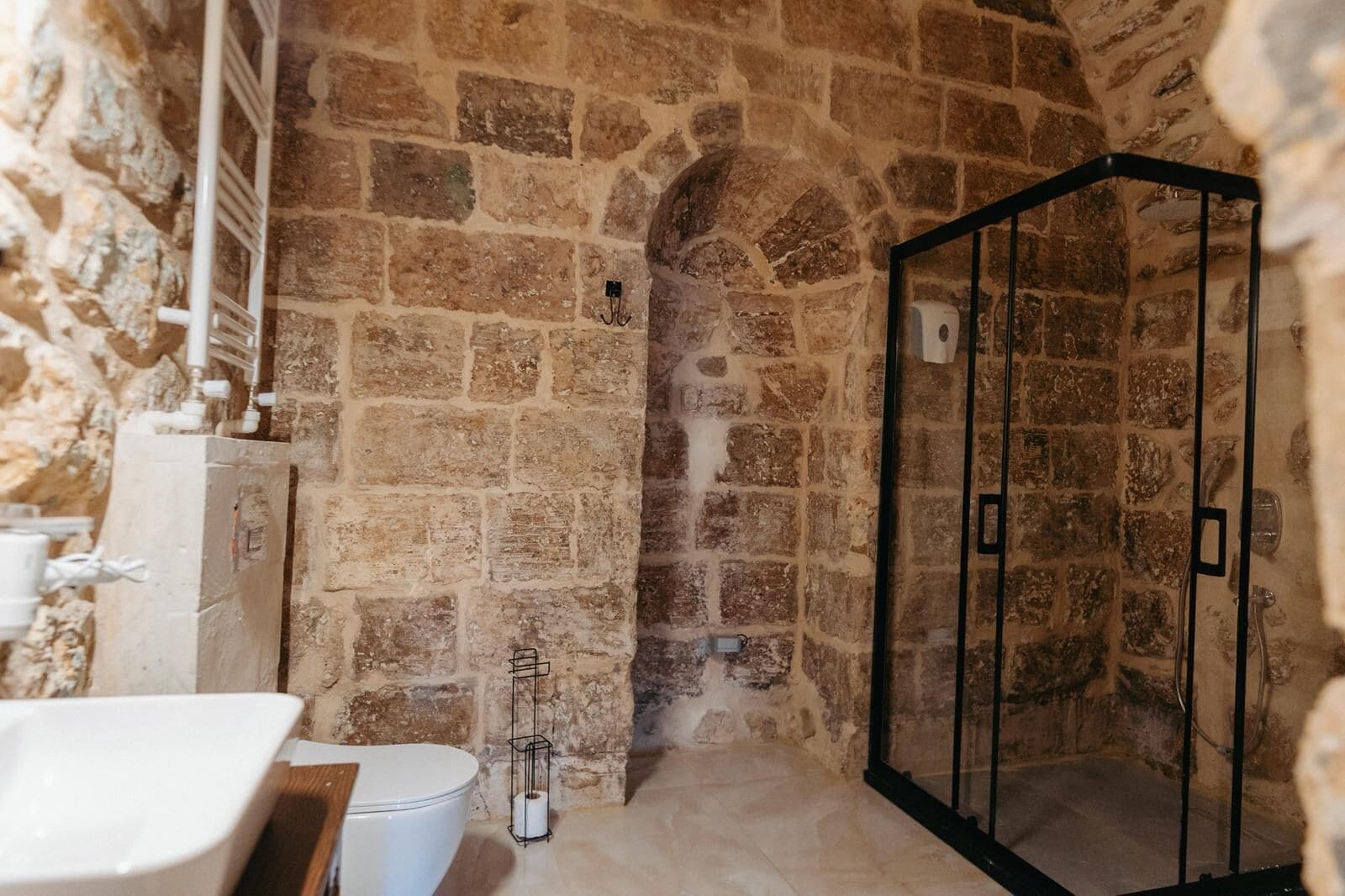 Une salle de bain aux murs en pierre, équipée d’une douche, de toilettes et d’un lavabo.
