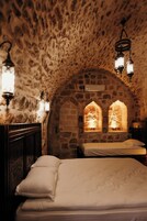 Una habitación de paredes de piedra con dos camas, un aparador de madera y lámparas fijadas a la pared.