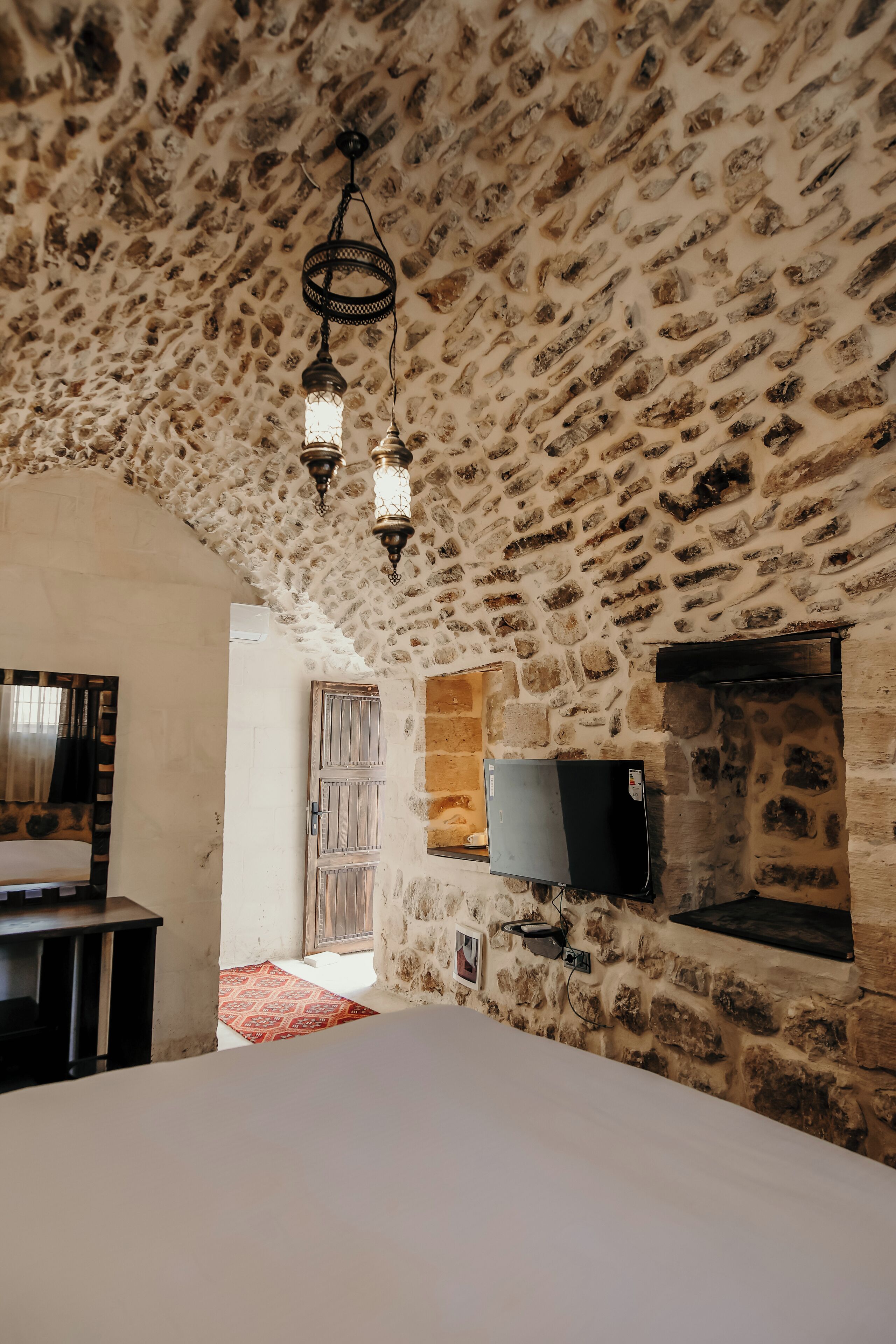 A room with a stone ceiling, a bed, a TV mounted on the wall, and a small window.