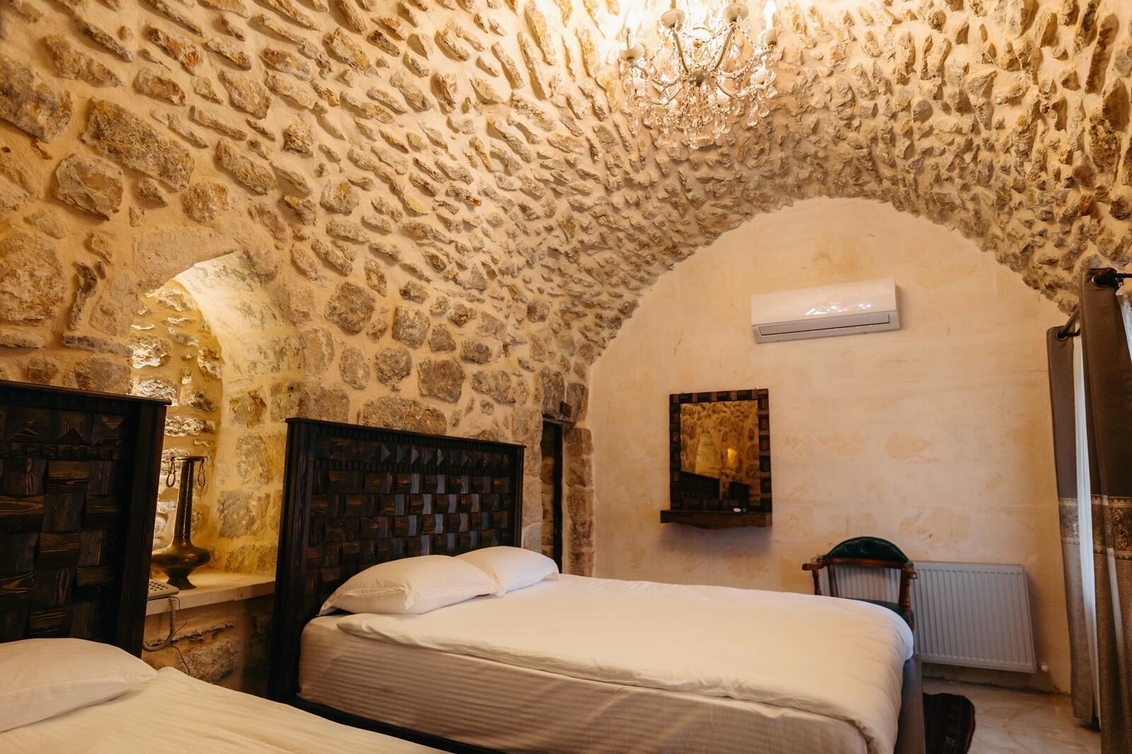 A room with a stone ceiling, a bed, a wooden headboard, a mirror, and an air conditioning unit.