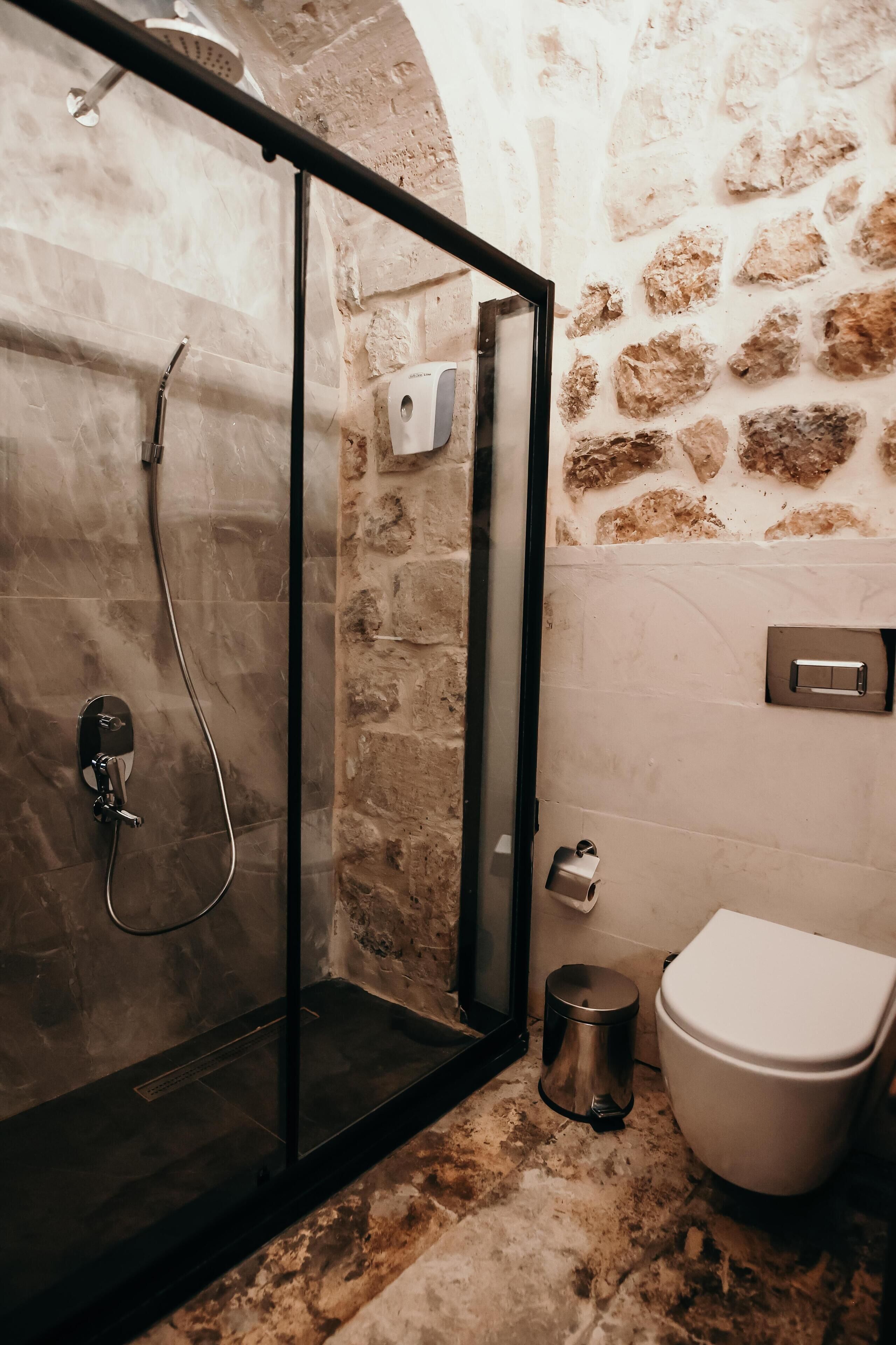 Et badeværelse med en brusekabine med glasvægge, et toilet og en skraldespand.