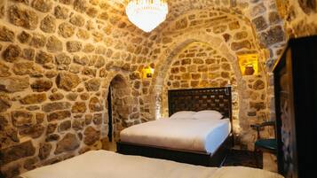 A stone-walled room with a bed, a chandelier, and two wall-mounted lights.
