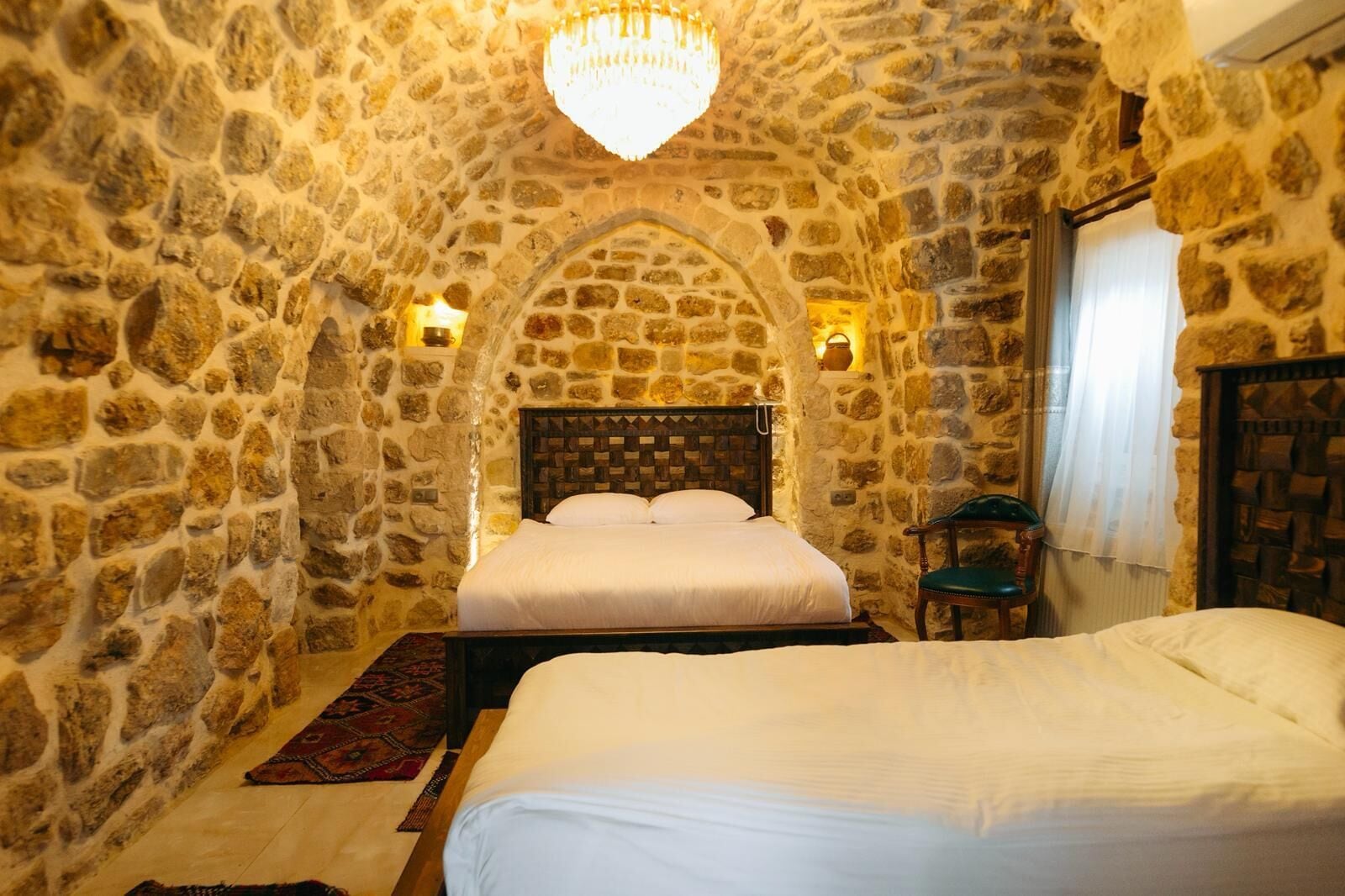 A stone-walled bedroom with a bed, a chair, and a chandelier.