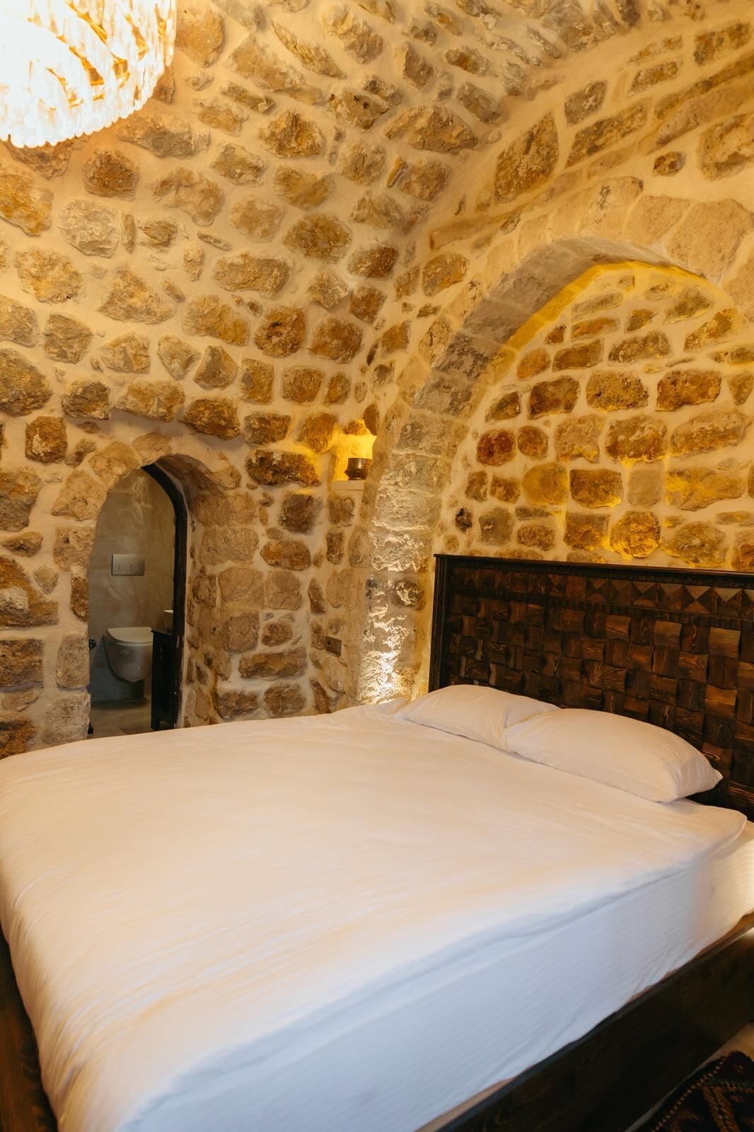 A stone-walled bedroom with a bed, an arched doorway, and a wooden headboard.