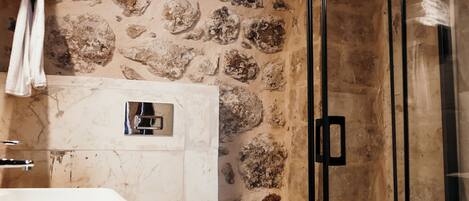 A bathroom with a stone wall, a glass shower enclosure, a white sink, and a toilet.