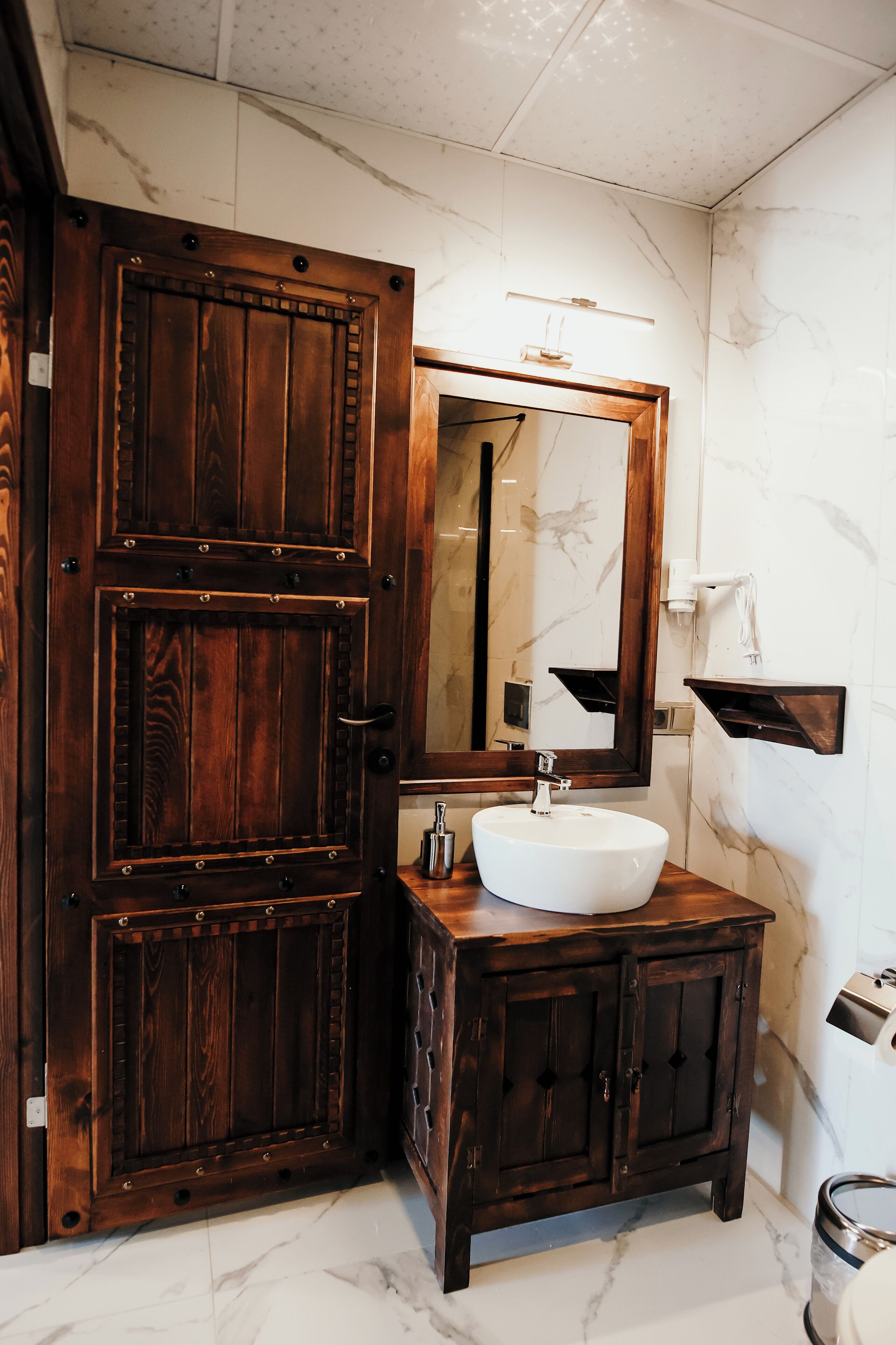 Un bagno con una porta in legno, un lavandino bianco e uno specchio.